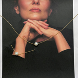 Model wearing Ina Necklace, closeup of pearl pendant on gold chain.
