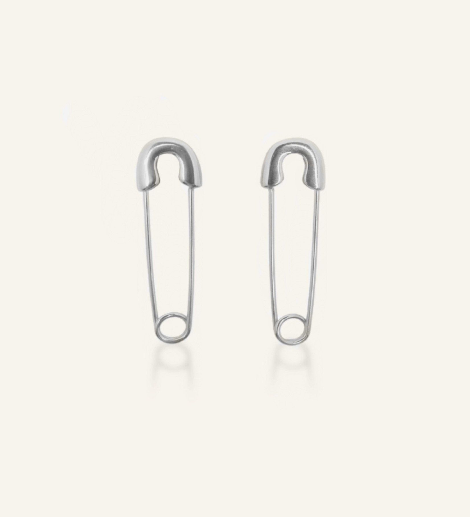 Silver-coated Gil Earrings designed like a safety pin, laid flat to show unique clasp and edgy shape.