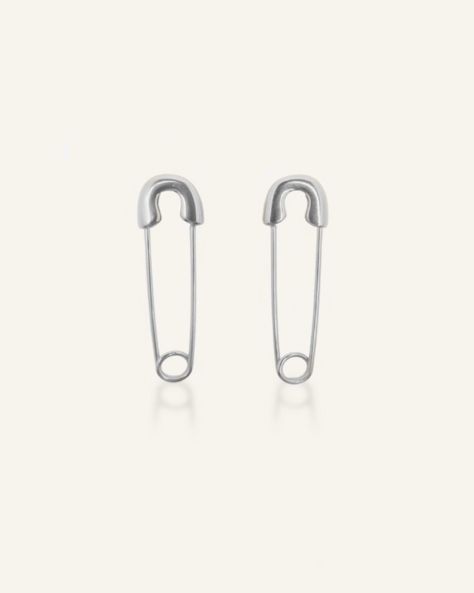 Silver-coated Gil Earrings designed like a safety pin, laid flat to show unique clasp and edgy shape.