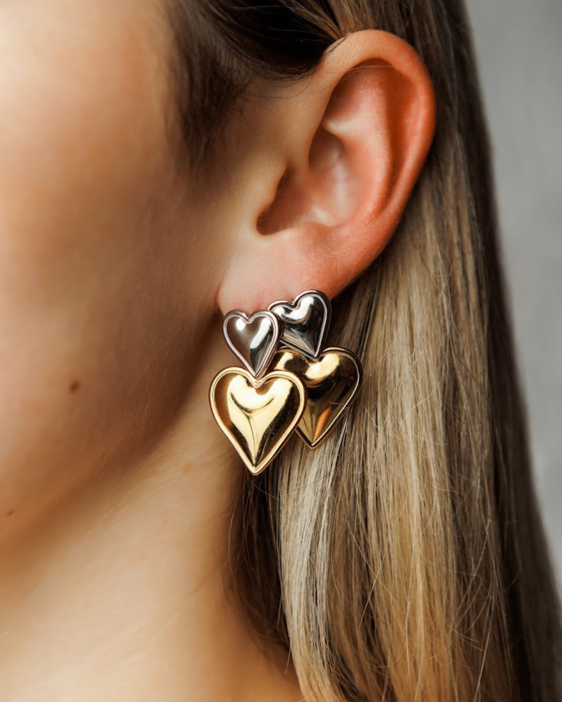 Close-up view of Giselle Earrings highlighting stacked heart detail in gold and silver.
