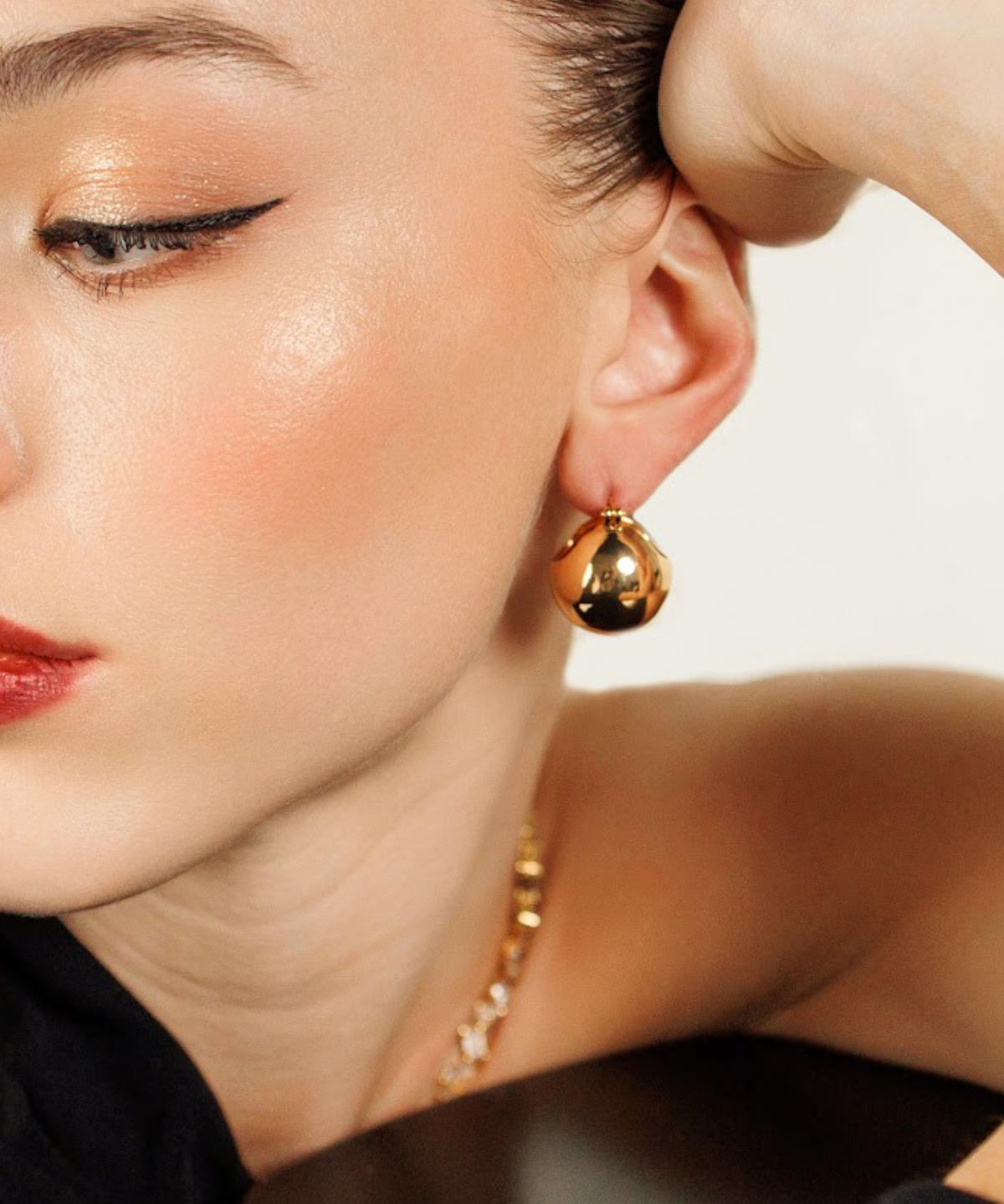 Close-up of model wearing Maeve Earrings in gold, showcasing dome shape and glossy texture.