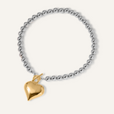 Flatlay of Margaux Necklace featuring a gold heart-shaped pendant and silver beaded chain.