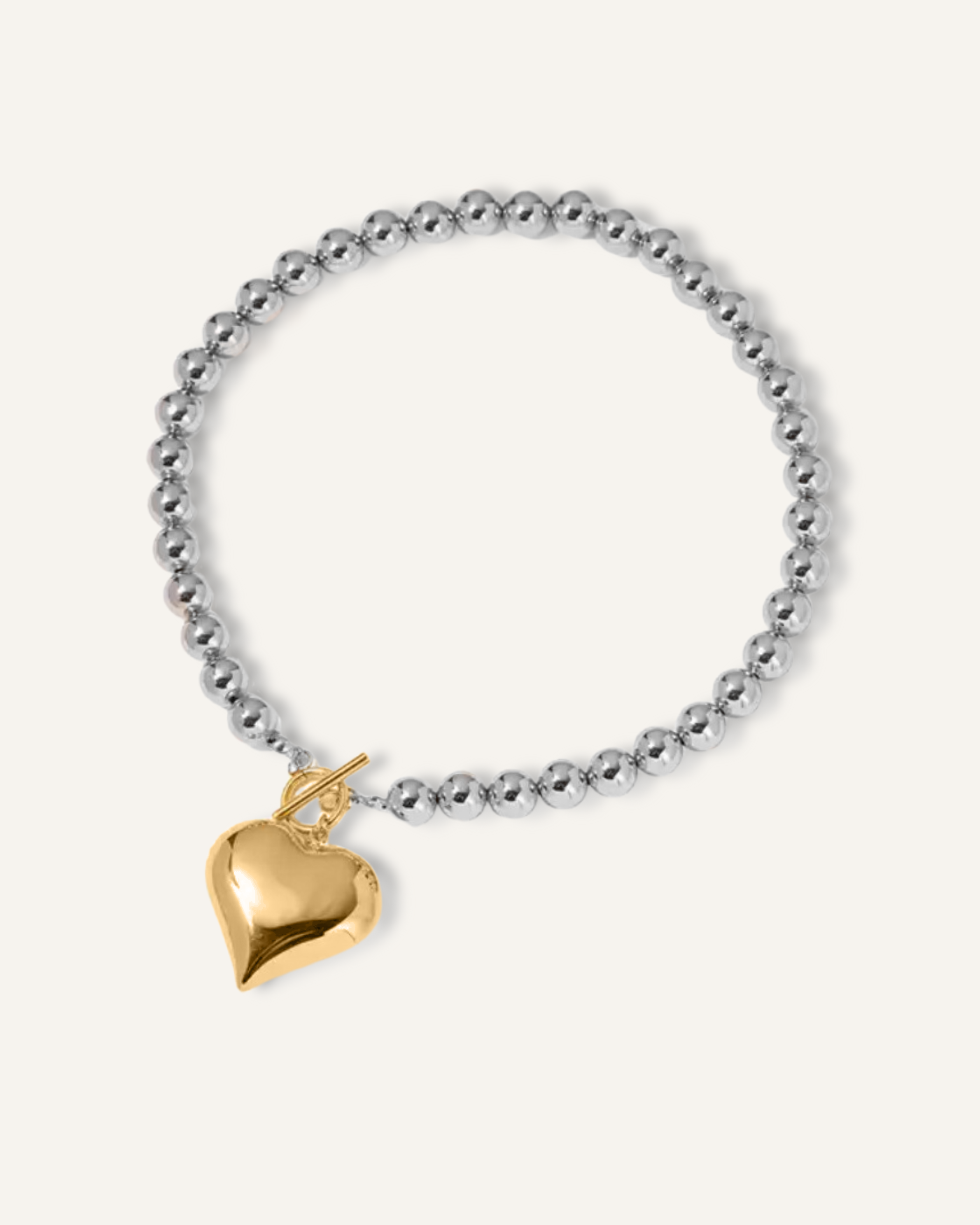 Flatlay of Margaux Necklace featuring a gold heart-shaped pendant and silver beaded chain.