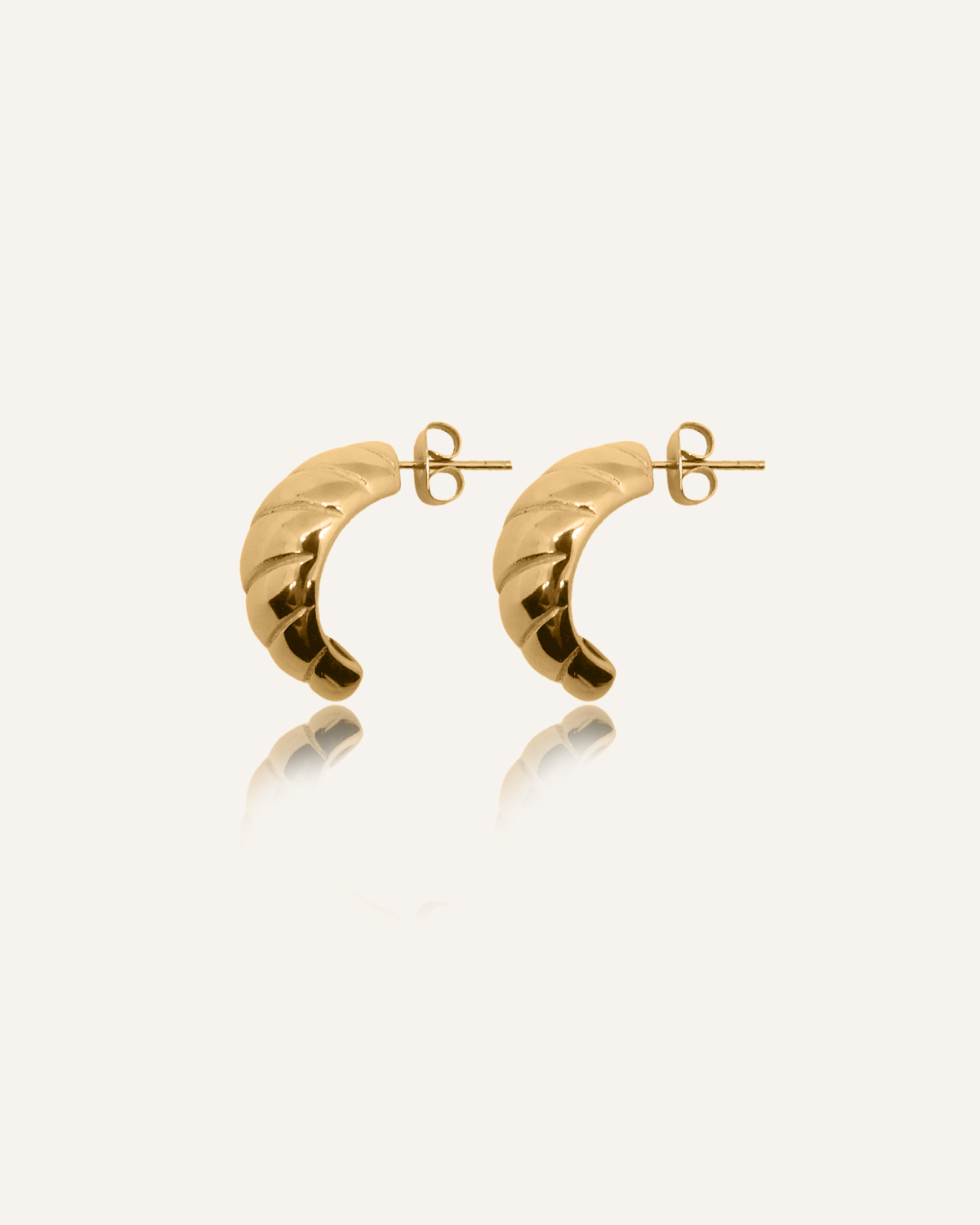 Flatlay of Mini Demi Earrings in 18k gold with croissant-inspired shape and glossy finish.