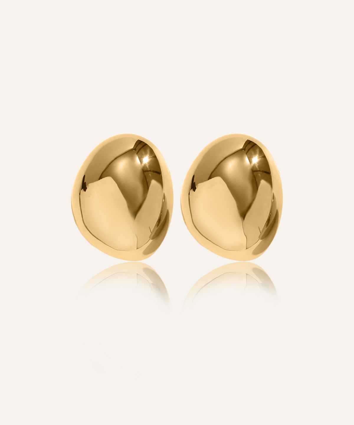 Mona Earrings in gold with bold imperfect oval dome design laid on white surface.