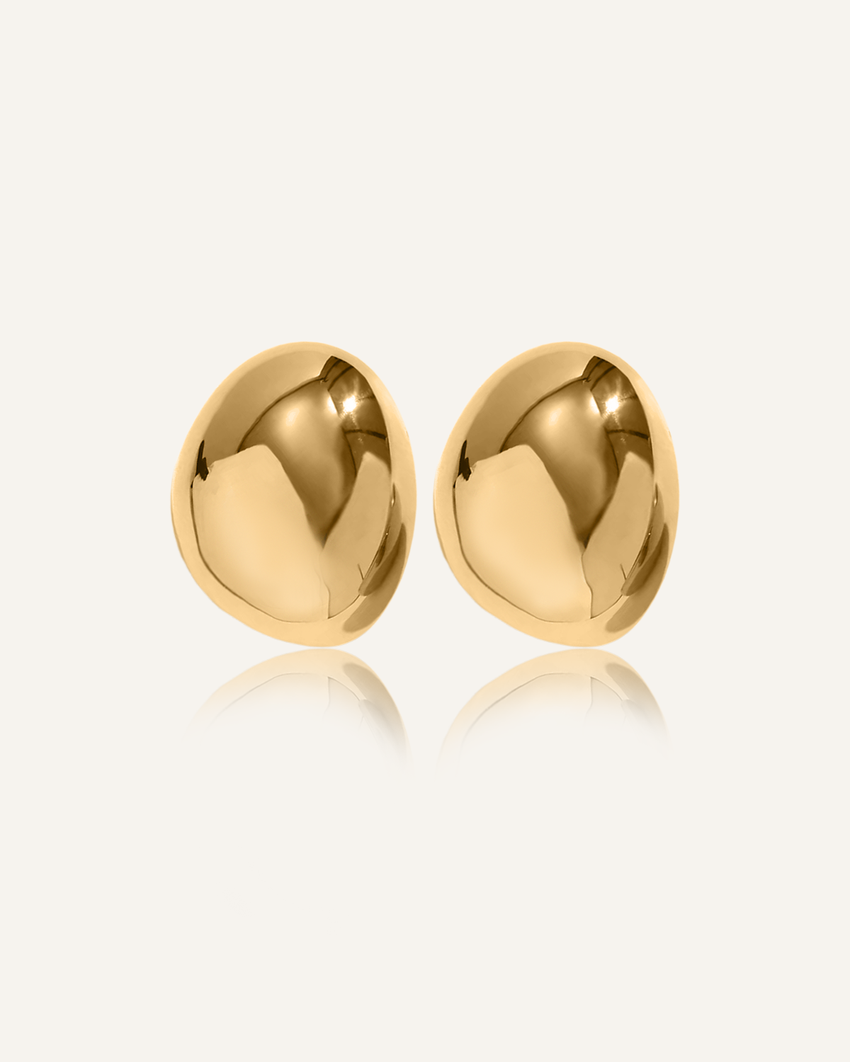 Mona Earrings in gold with bold imperfect oval dome design laid on white surface.