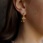 Close-up of Tyla Earrings worn on ear, showcasing gold texture with pearl and zirconia detail.