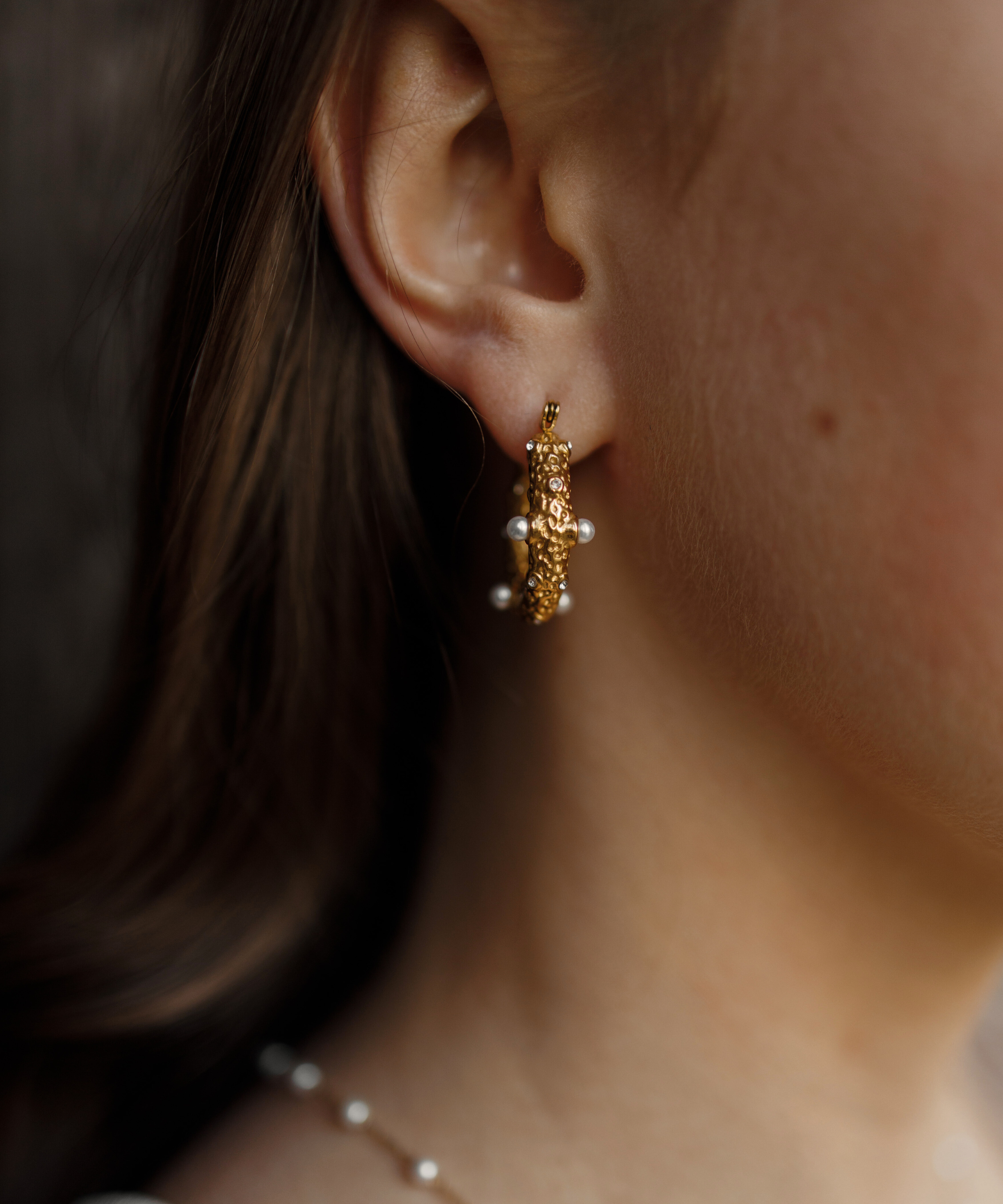 Close-up of Tyla Earrings worn on ear, showcasing gold texture with pearl and zirconia detail.