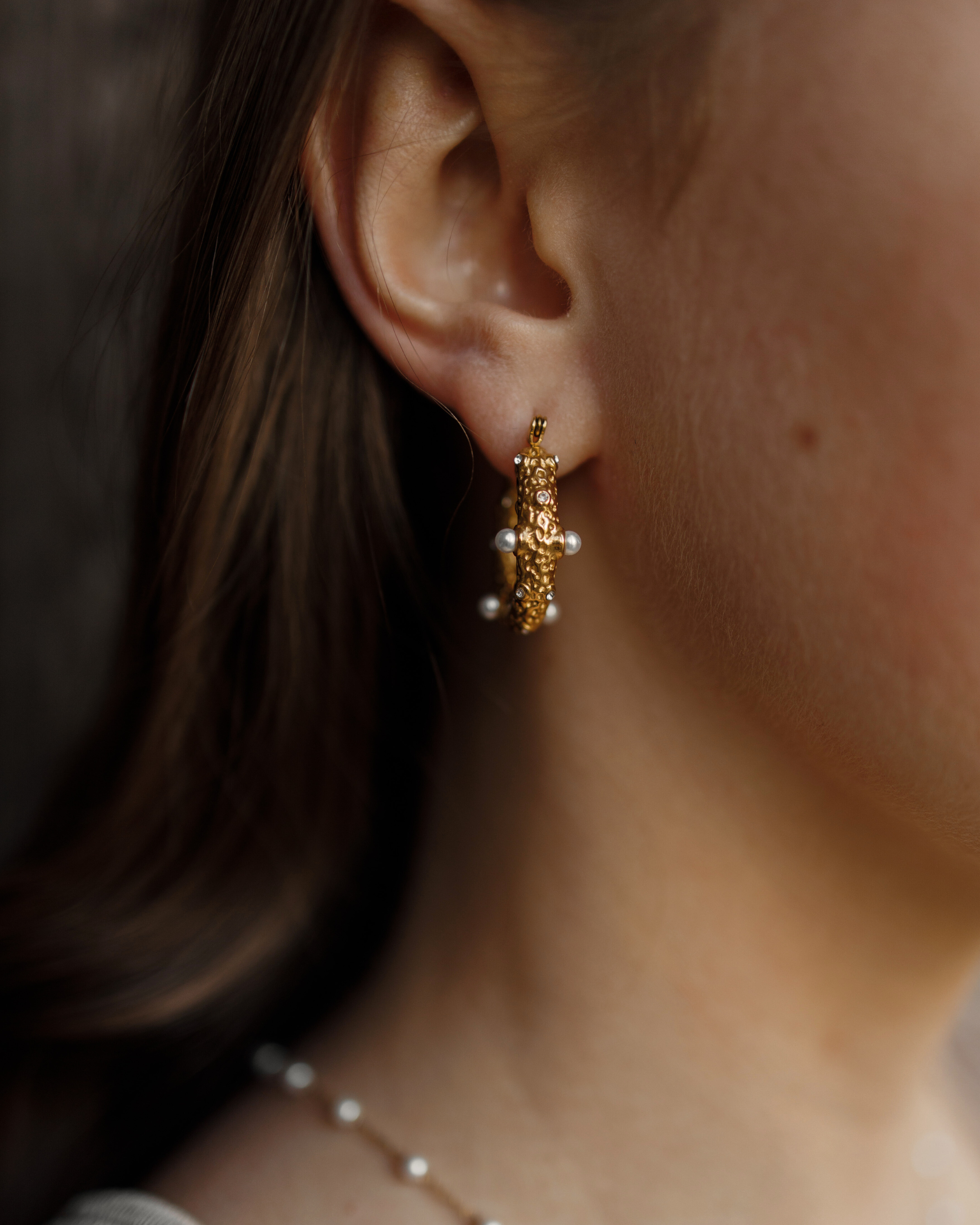 Close-up of Tyla Earrings worn on ear, showcasing gold texture with pearl and zirconia detail.