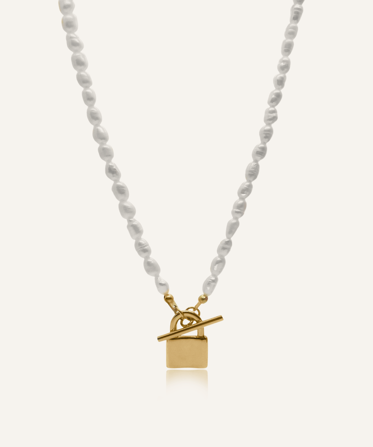 Lily Necklace flatlay showing freshwater pearls and gold padlock pendant with toggle closure.