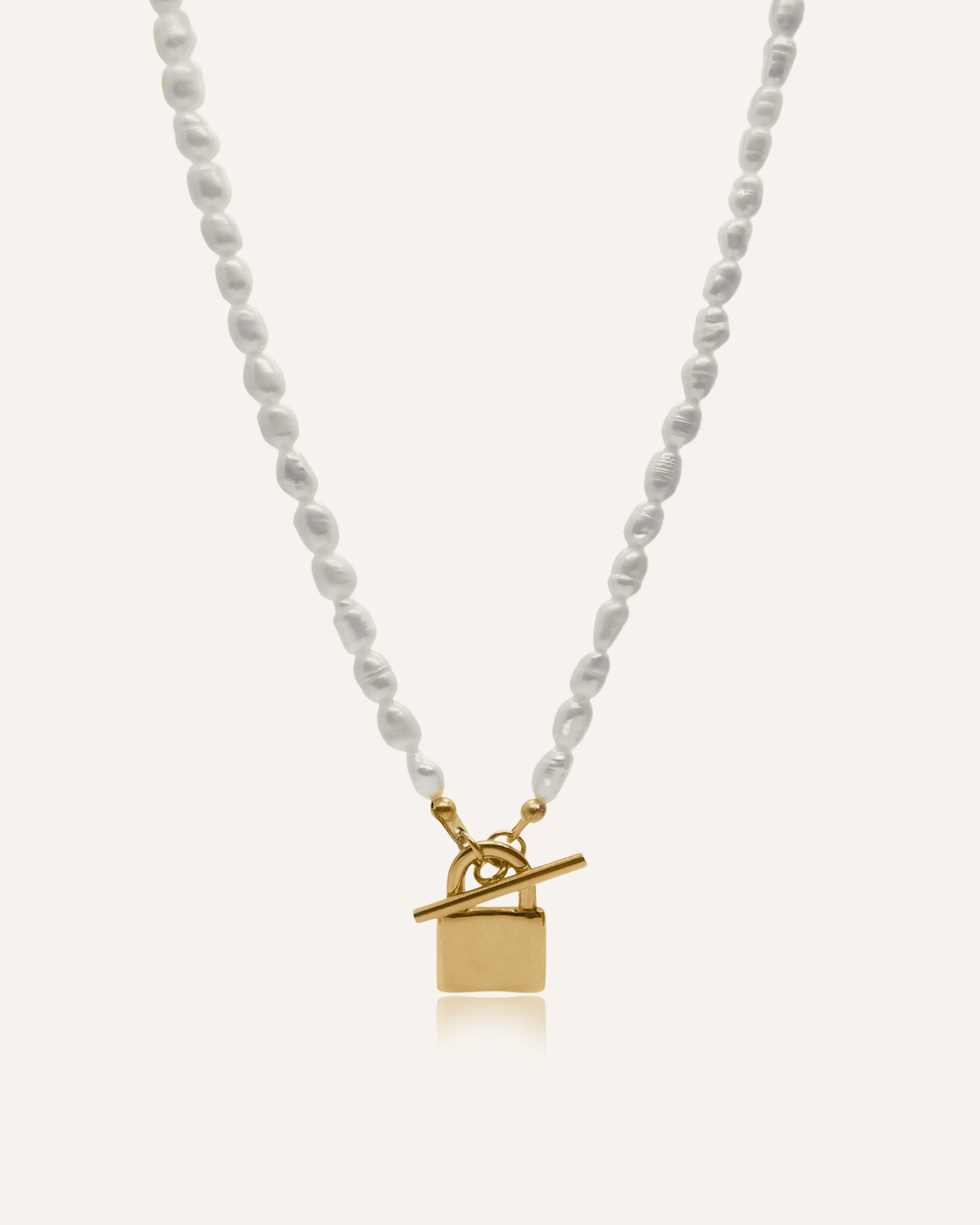 Lily Necklace flatlay showing freshwater pearls and gold padlock pendant with toggle closure.